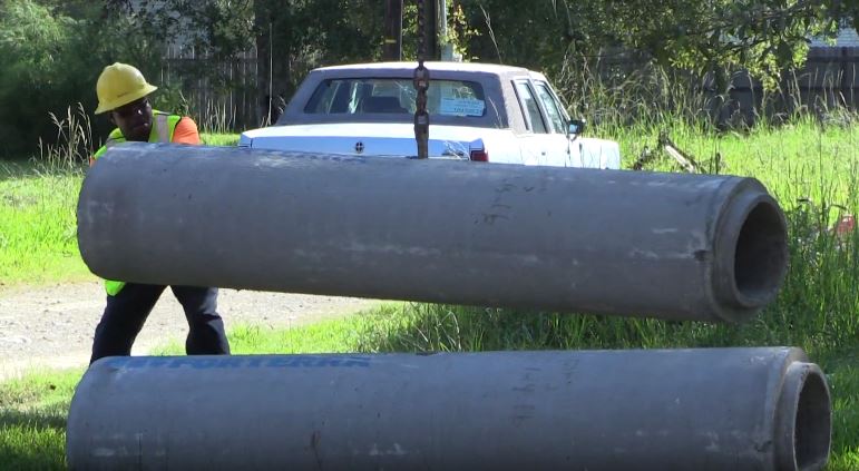 PW employee guiding concrete pipes for drainage